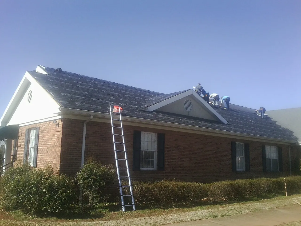 Crew tearing shingles off a brick ranch roof with a ladder set — Emergency Roof Repair work by our crew in Palo