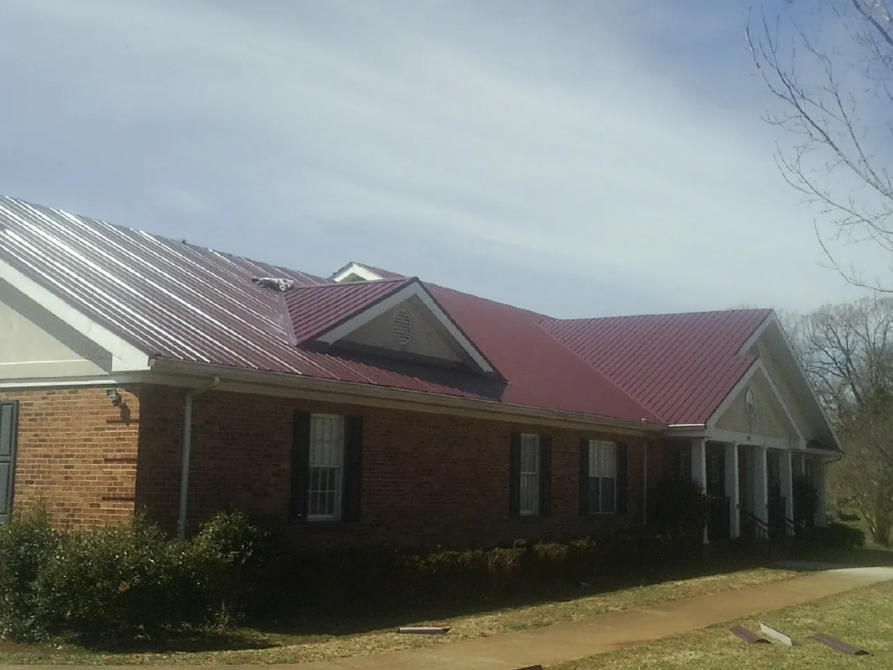 Red metal roof with gabled entries on a long brick building, from a Hail Damage Roof Repair job in Palo