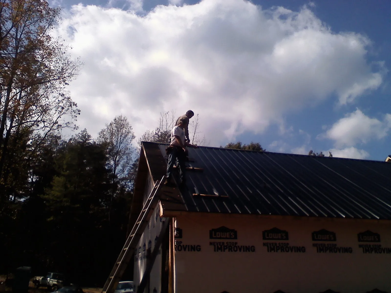 Roofer fastening dark metal panels high against a cloudy sky, from a Roof Inspection job in Palo
