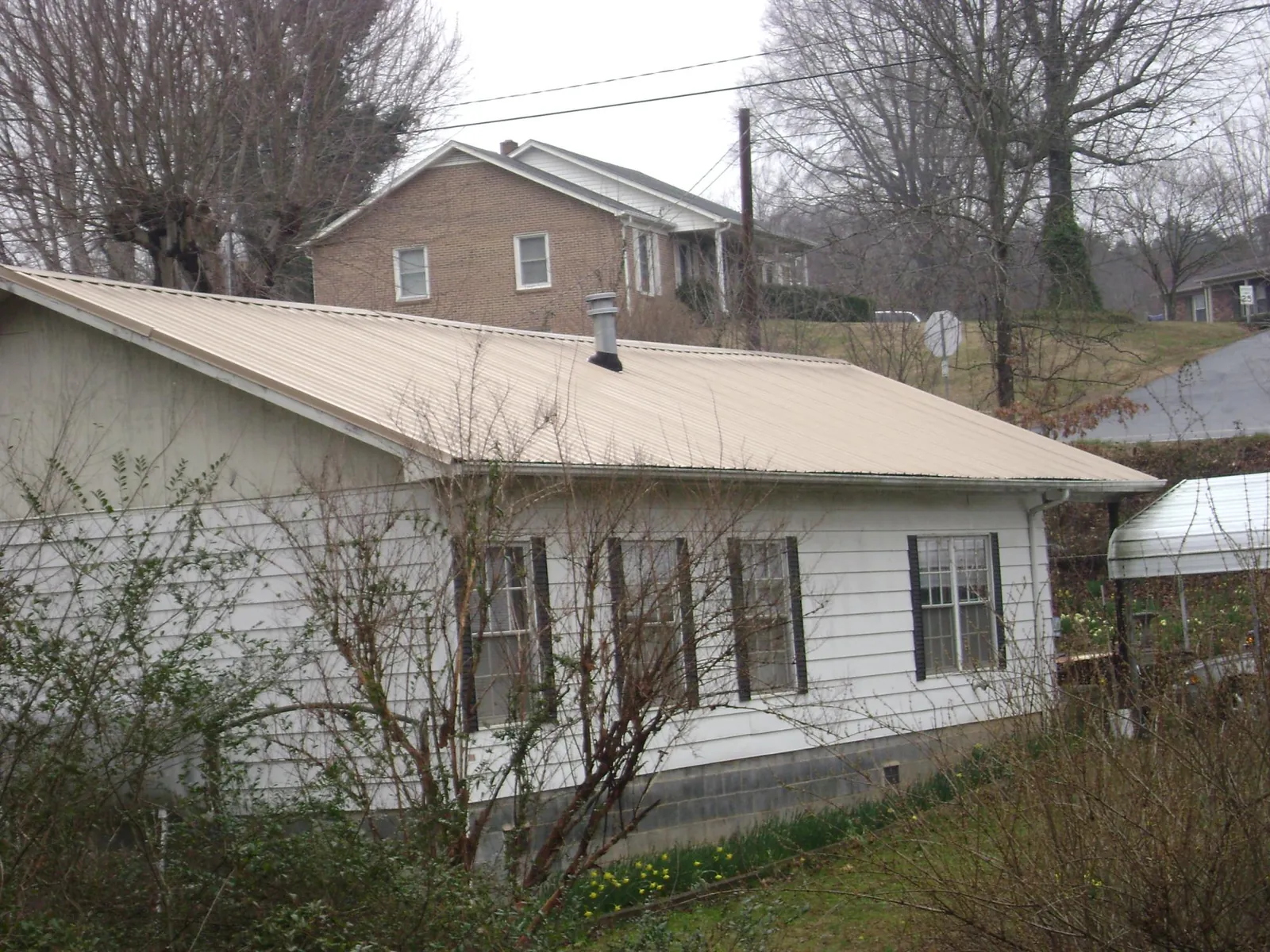 Tan metal roof on a white sided house set into a hillside — Commercial Roofing by Roofing Brothers in Palo